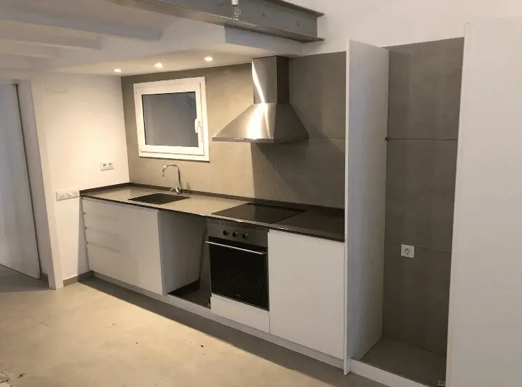 Reforma de cocina lineal con mobiliario blanco y revestimiento cerámico gris en Barcelona
