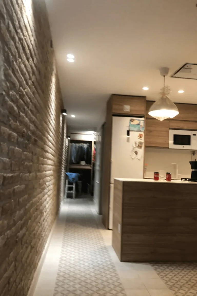 Pasillo con pared de ladrillo visto e iluminación LED hacia vestidor en reforma en Barcelona