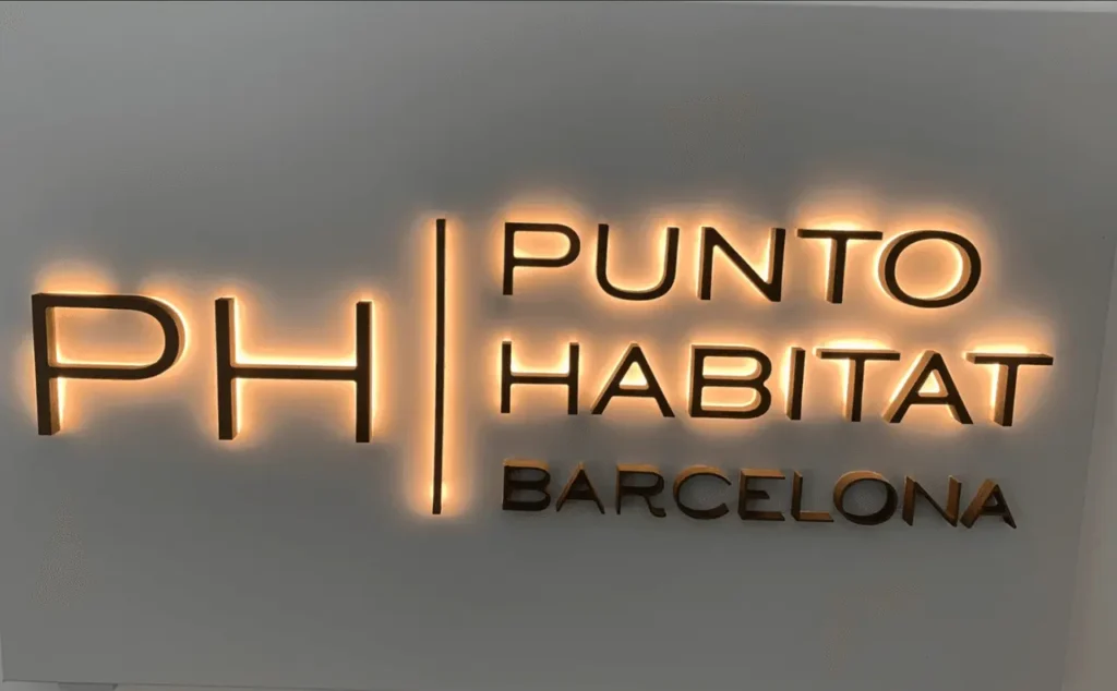 Rótulo de oficina con letras metálicas retroiluminadas montadas sobre pared lisa blanca.