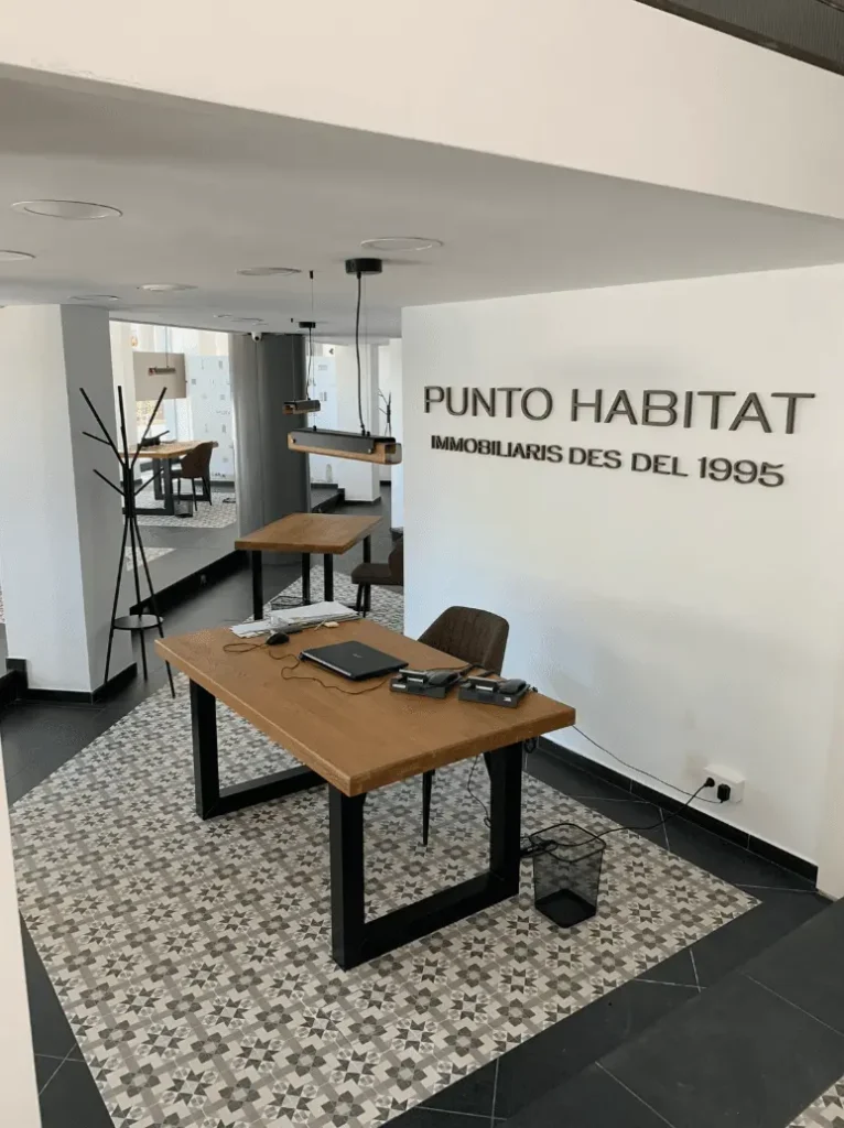 Oficina moderna con suelo de baldosa hidráulica, paredes blancas y mesas de madera natural con estructura metálica.