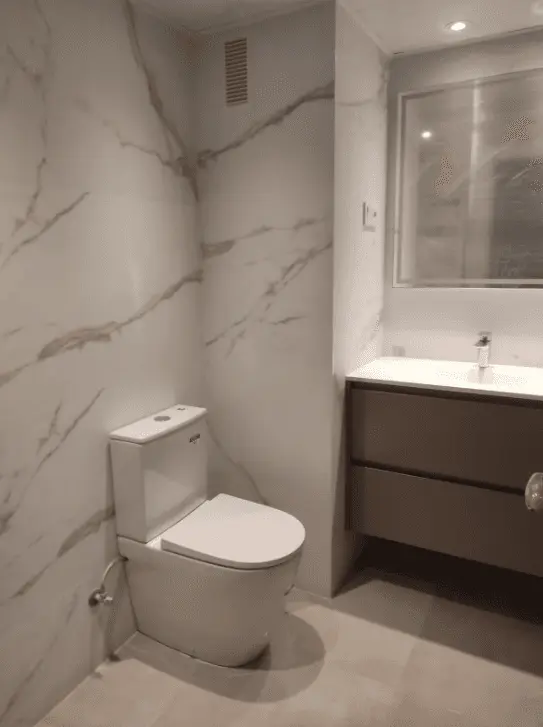 Baño moderno con sanitario de líneas rectas, lavabo suspendido y revestimiento de mármol blanco veteado.