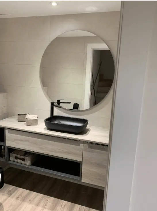 Vista del lavamanos negro con grifo monomando y espejo redondo de gran tamaño en un baño reformado con estilo moderno, interior lavabo Can Boira.
