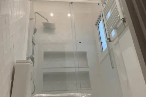 Baño moderno con ducha acristalada, estanterías empotradas y techo rústico con vigas de madera.