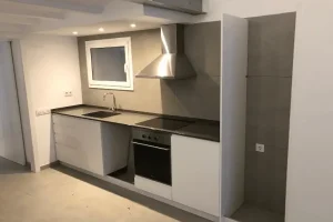 Reforma de cocina lineal con mobiliario blanco y revestimiento cerámico gris en Barcelona
