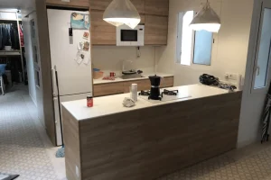 Cocina office reformada con barra de madera, encimera blanca y mobiliario a medida.