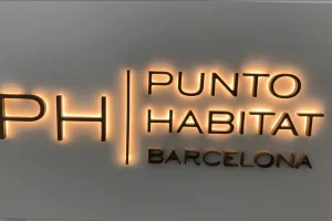 Rótulo de oficina con letras metálicas retroiluminadas montadas sobre pared lisa blanca.