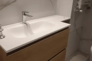 Lavamanos doble con encimera blanca y mueble inferior de madera natural, grifo monomando cromado y espejo grande.