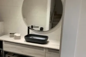 Vista del lavamanos negro con grifo monomando y espejo redondo de gran tamaño en un baño reformado con estilo moderno, interior lavabo Can Boira.