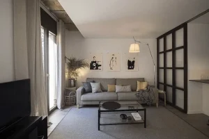 Salón moderno en Barcelona con sofá gris, pared de arte minimalista y separación de cristal y madera.