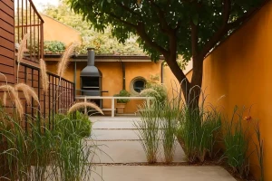 Patio exterior con sendero de hormigón, vegetación ornamental y paredes pintadas en tonos ocres.