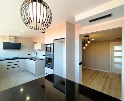 Cocina reformada de estilo moderno con acabados en madera clara y encimeras negras.