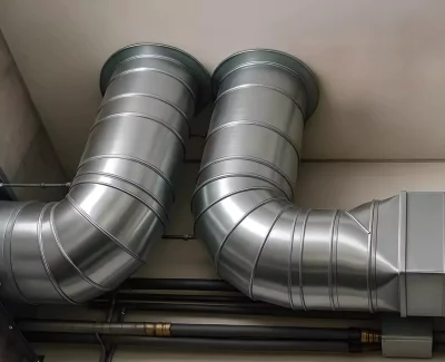 Conductos metálicos de ventilación en sistema de climatización industrial instalados en pared técnica.